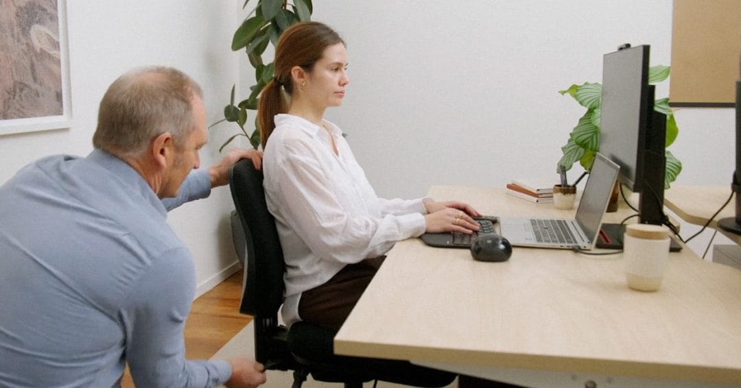 ergonomist adjusting woman's office chair and posture