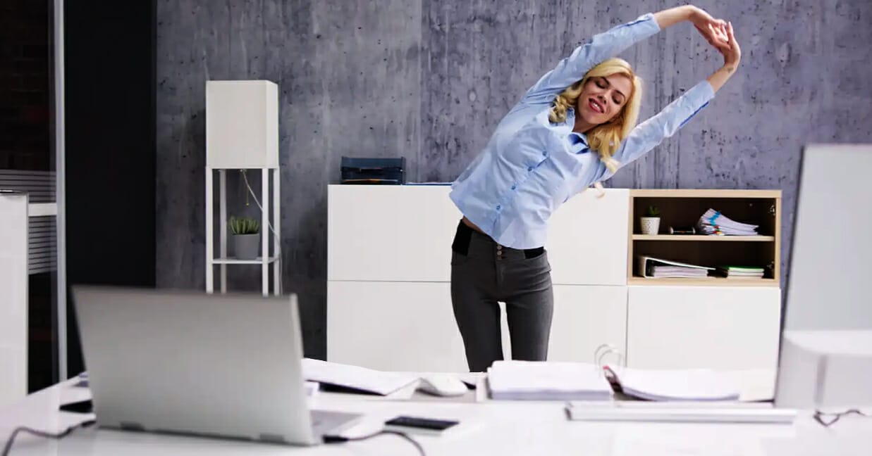 A woman with good work-from-home ergonomics, taking a break to stretch.